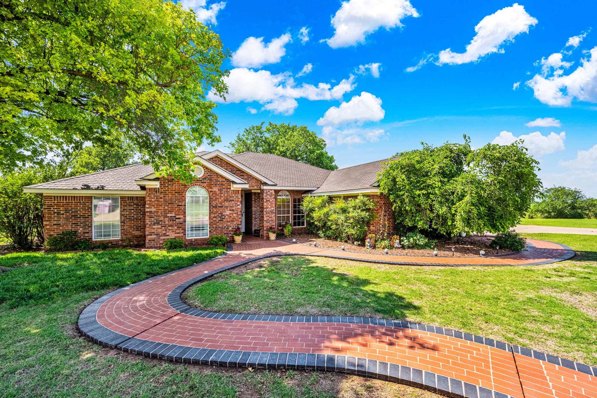 Front exterior of a brick ranch estate home in Chickasha — established landscaping with a curving brick walkway and decorative stonework