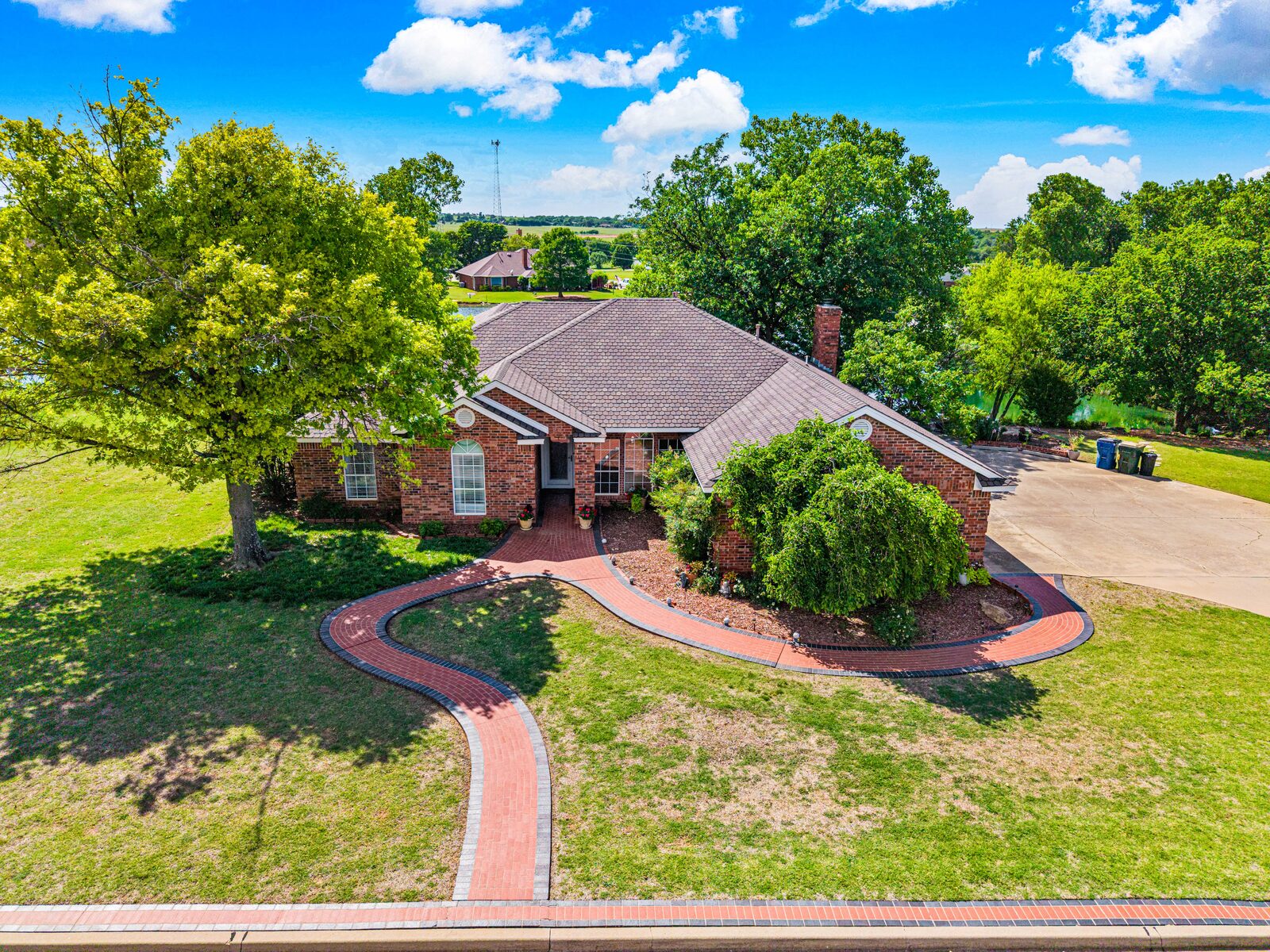 Aerial view of the home and front grounds showing the brick exterior, mature trees, and approach