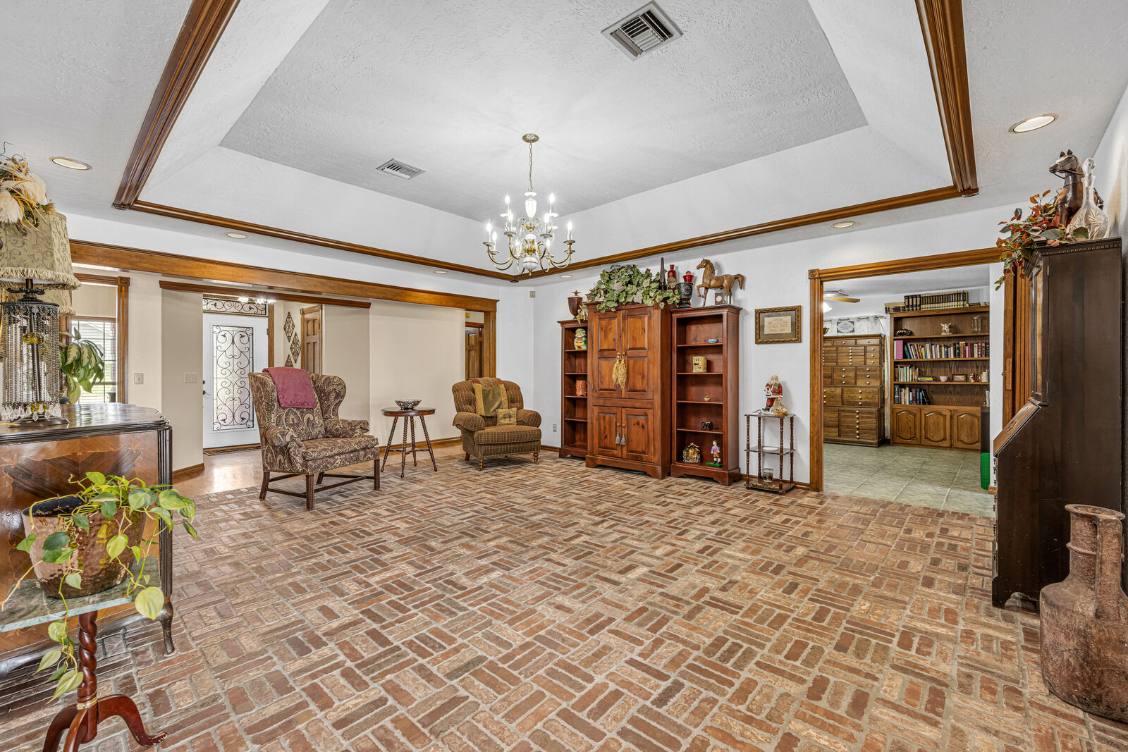 Formal living area with a tray ceiling, stained wood crown molding, brick flooring, and built-in wooden cabinetry