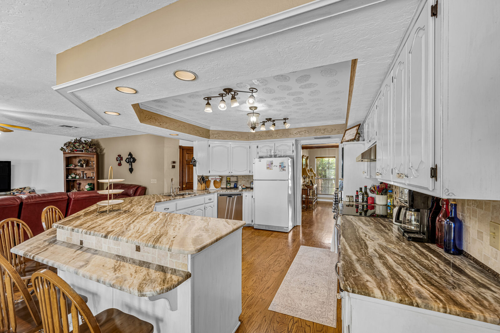 Kitchen with white cabinetry, natural stone counters, breakfast bar seating, and track lighting opening into the living spaces