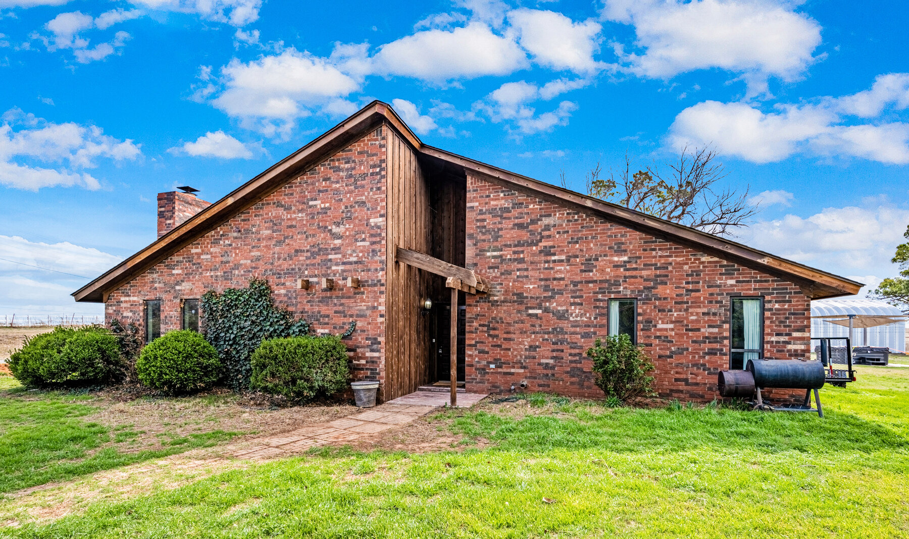 Front exterior of a brick country home in Chickasha — distinctive A-frame profile with a stained wood accent at the peak and a brick chimney