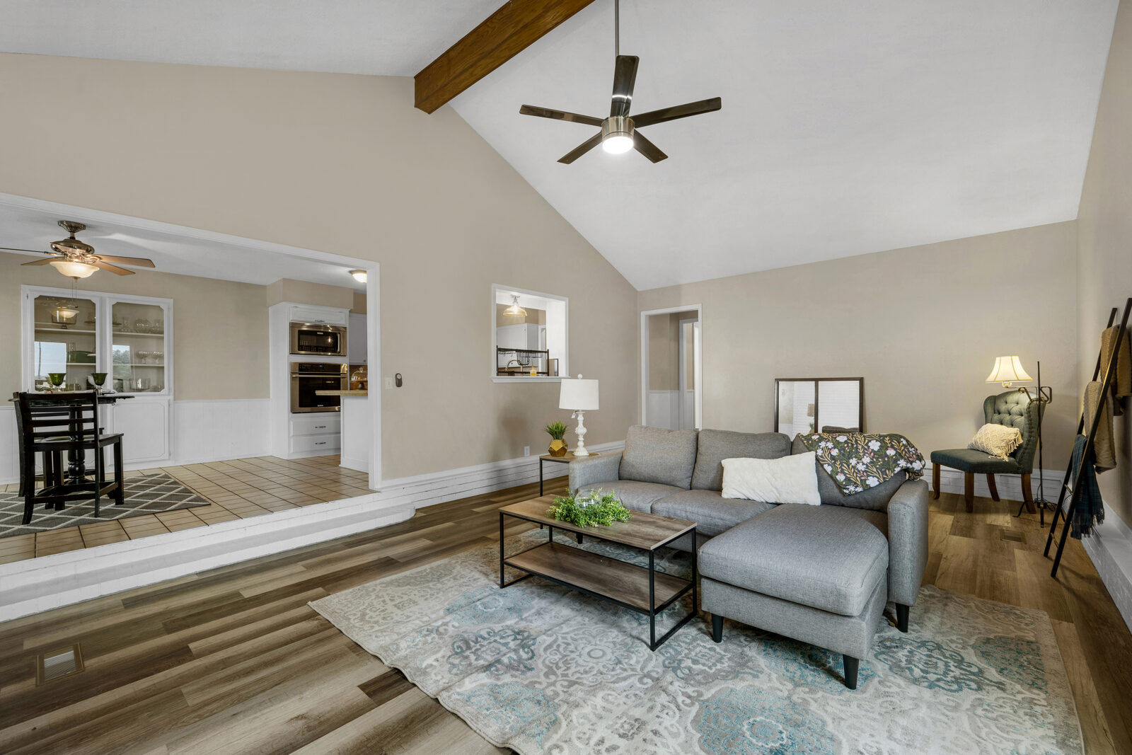 Sunken living room transitioning up to the dining area with built-in cabinetry — vaulted ceiling with wood beam, view through to the kitchen beyond