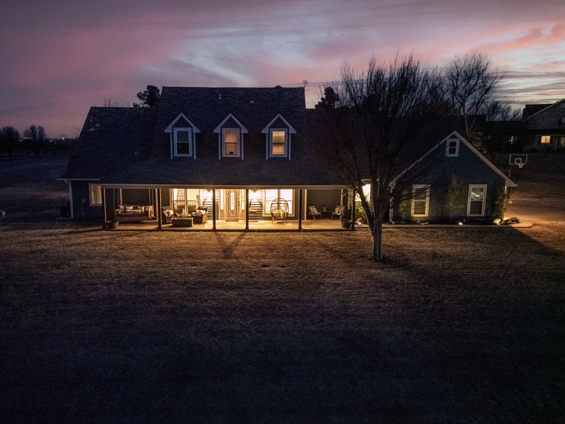 Modern farmhouse in Chickasha at twilight — drone shot with glowing windows