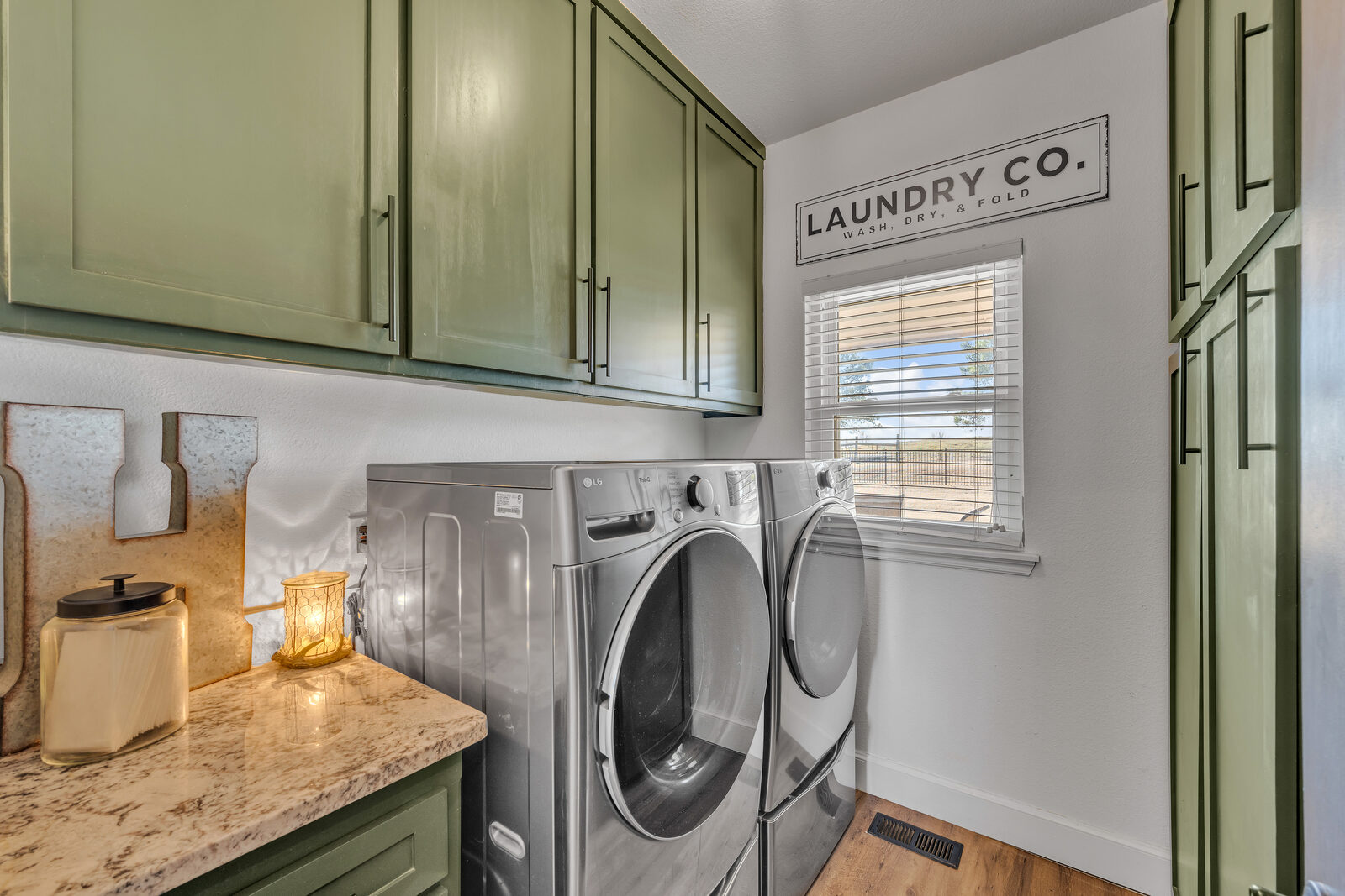Laundry room with sage green shaker cabinetry, granite counter, front-load stacked-set appliances, and a window with a countryside view