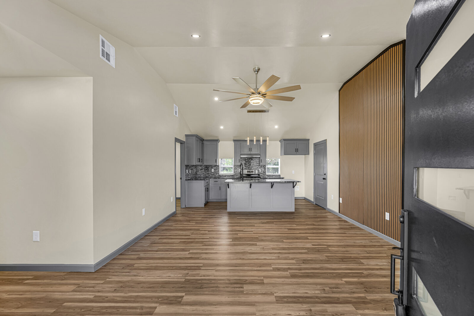 Open-concept living and kitchen with vaulted ceiling, gray cabinetry, wood slat accent wall, and pendant lighting over the island