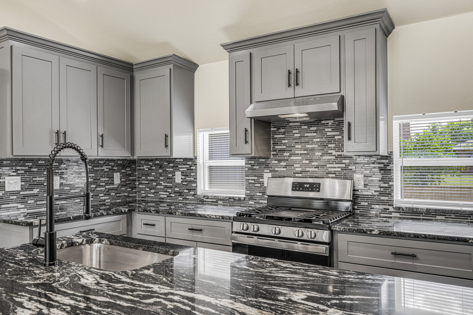 Kitchen detail — gray shaker cabinets, black granite countertops, gas range, gray glass mosaic backsplash