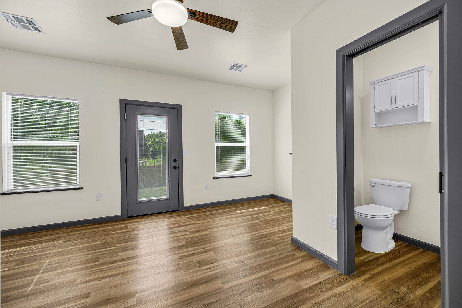 Primary bedroom — wood flooring, French door to the backyard, ensuite bathroom visible through an open doorway