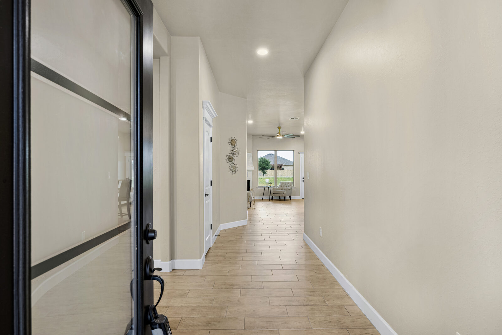 Entry foyer looking down a long hallway to the staged living area, wood-look tile flooring throughout