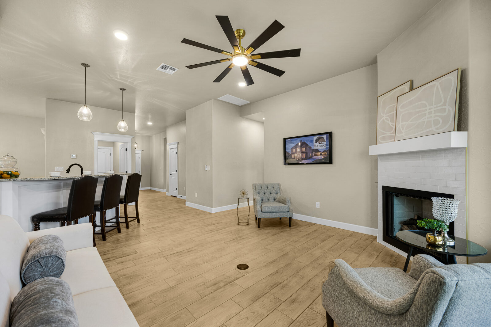 Living room with white subway tile fireplace surround, modern ceiling fan, and open passage back to the kitchen and dining area