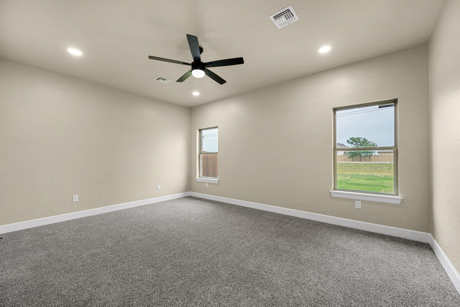 Secondary bedroom with plush gray carpet, ceiling fan, and two windows