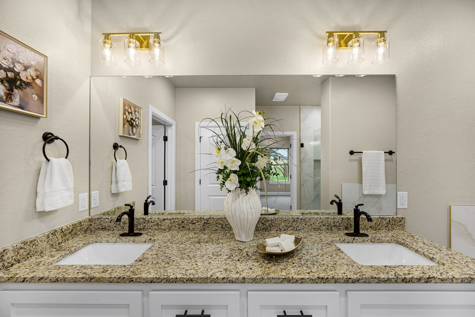 Primary bathroom double vanity with granite counters, square undermount sinks, brass vanity light bars, and oil-rubbed bronze faucets
