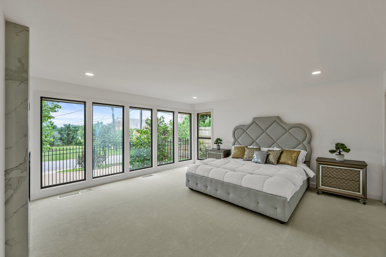 Primary bedroom with a wall of black-framed picture windows overlooking the gardens, oversized tufted velvet headboard, and mirrored bedside cabinetry