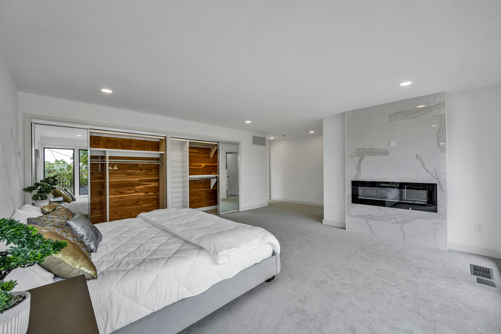 Primary suite with its own white marble fireplace, dual cedar-lined walk-in closets behind mirrored sliding doors, light carpet, and recessed lighting throughout