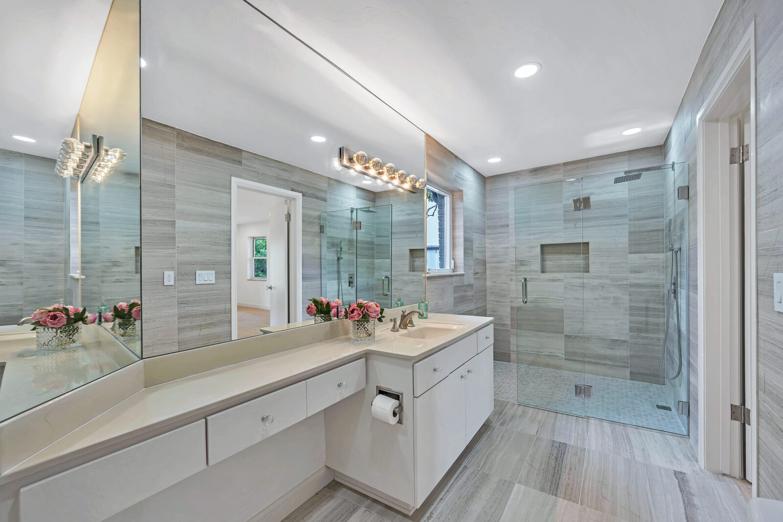 Secondary bath with gray stone-look porcelain tile floor-to-ceiling, a frameless glass walk-in shower with rain head, floating white vanity, and a crystal bubble sconce