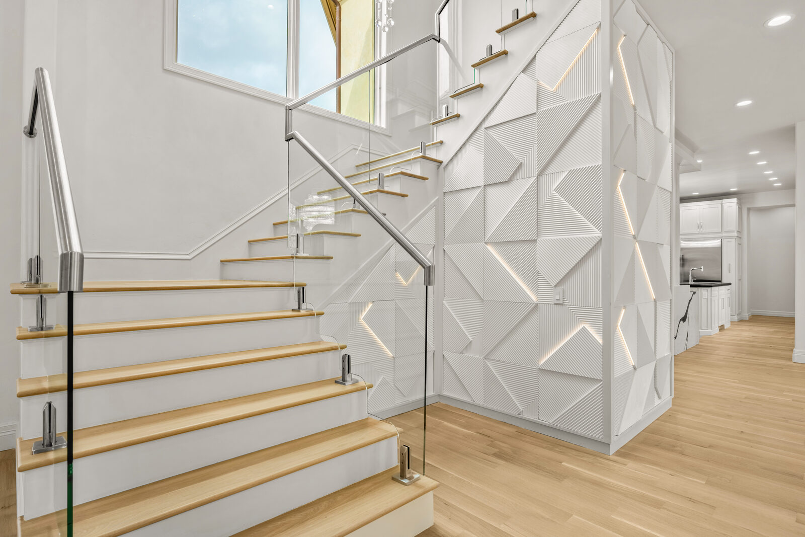 Contemporary open staircase with glass railings, light oak treads on white risers, set against a 3D textured accent wall with integrated LED accent lighting